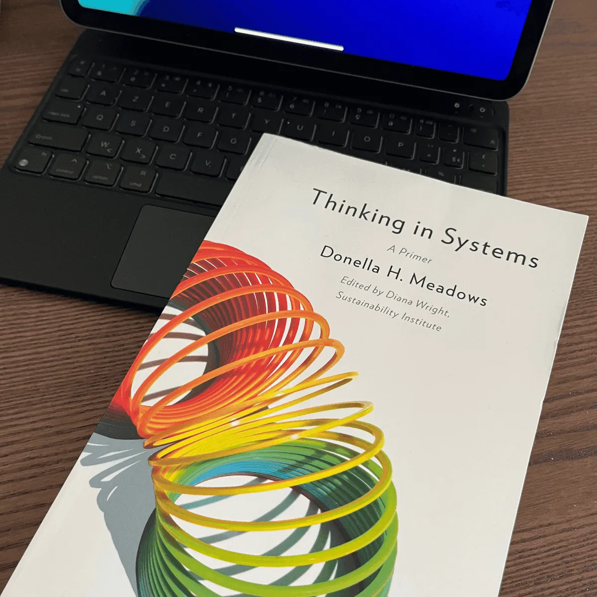 Het boek Thinking in Systems van Donella H. Meadows op een bureau naast een tablet met toetsenbord